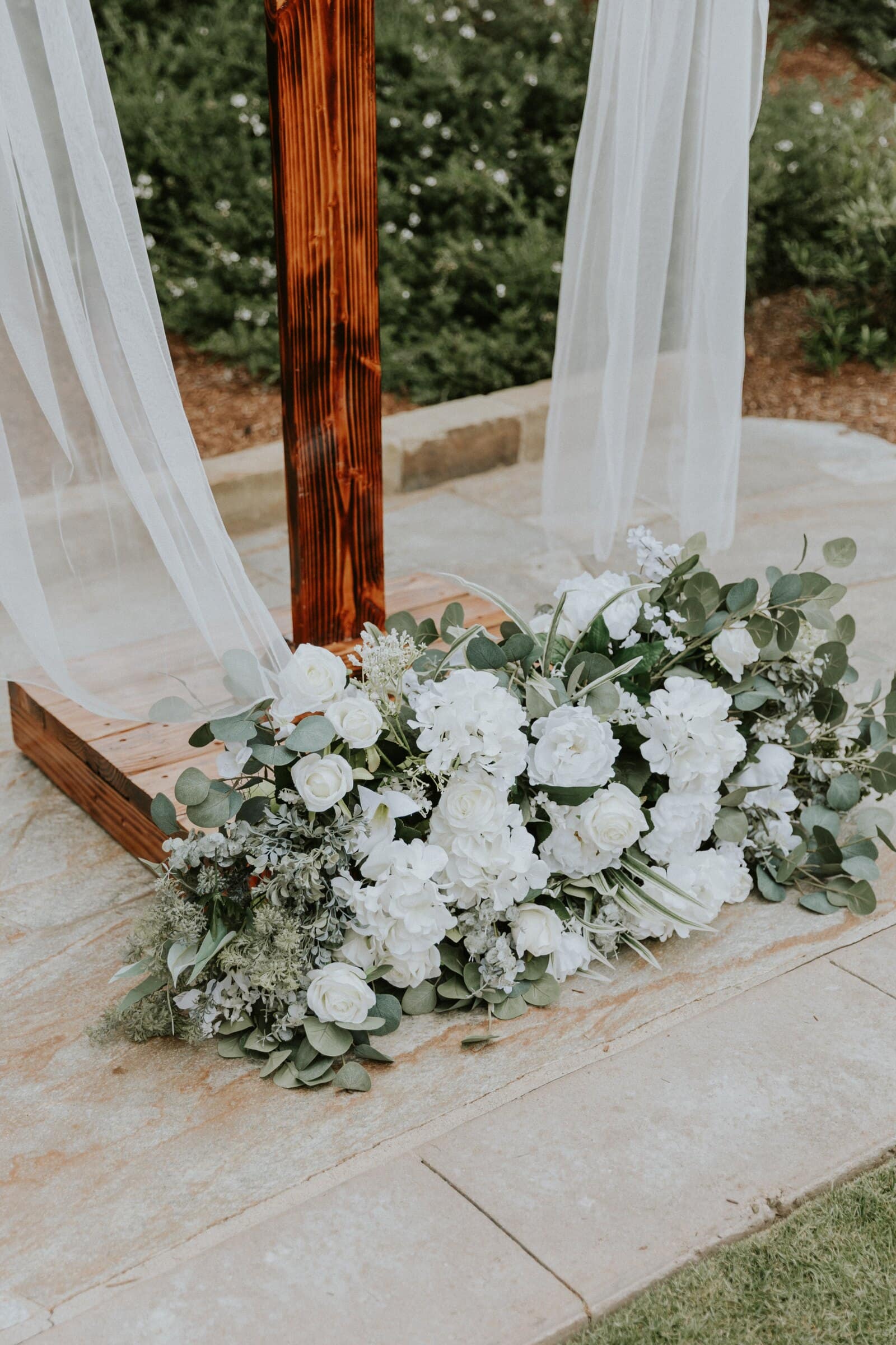 White hydrangeas and greenery at the foot of the ceremony arch