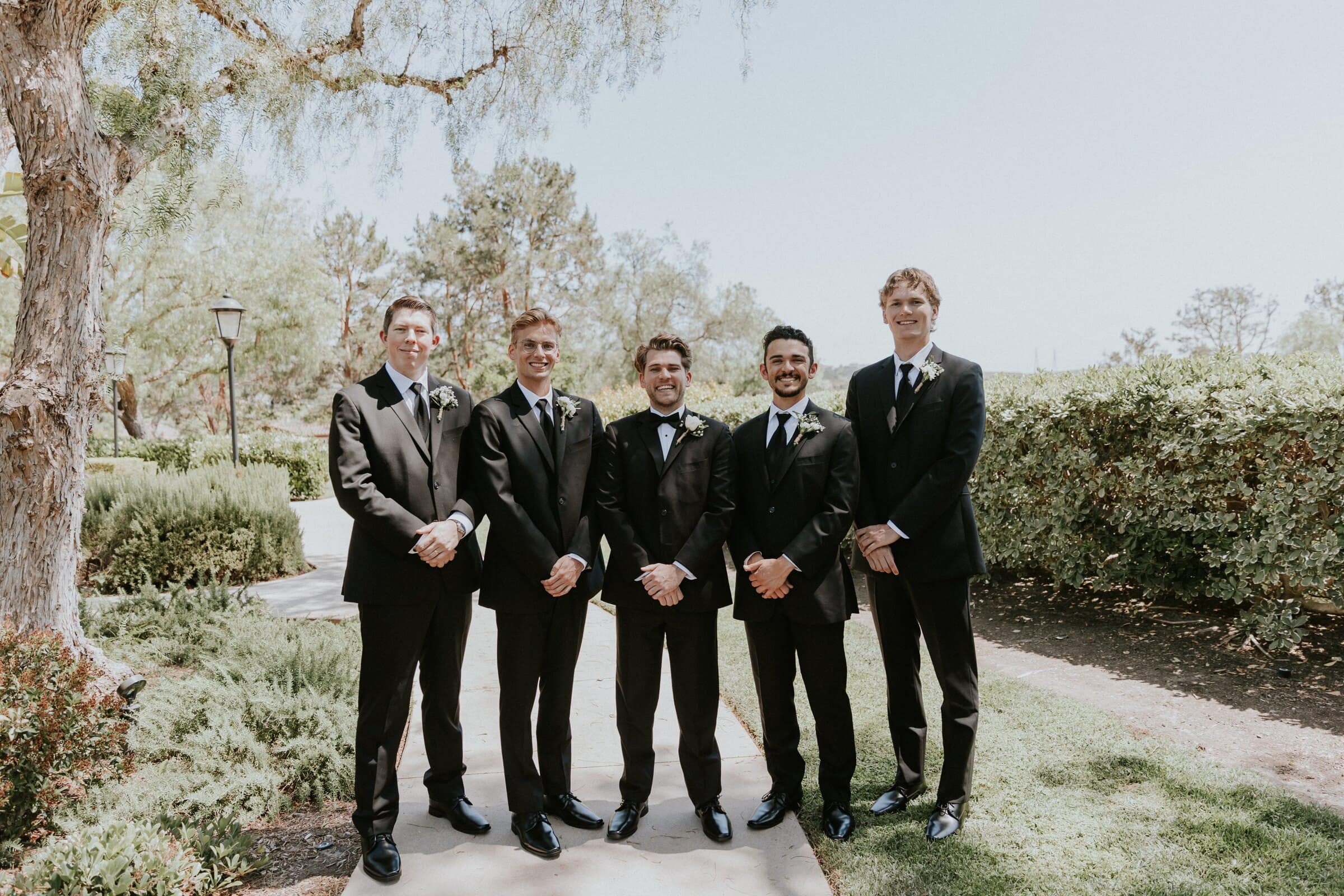 The groomsmen in black tuxedos lined up in the garden