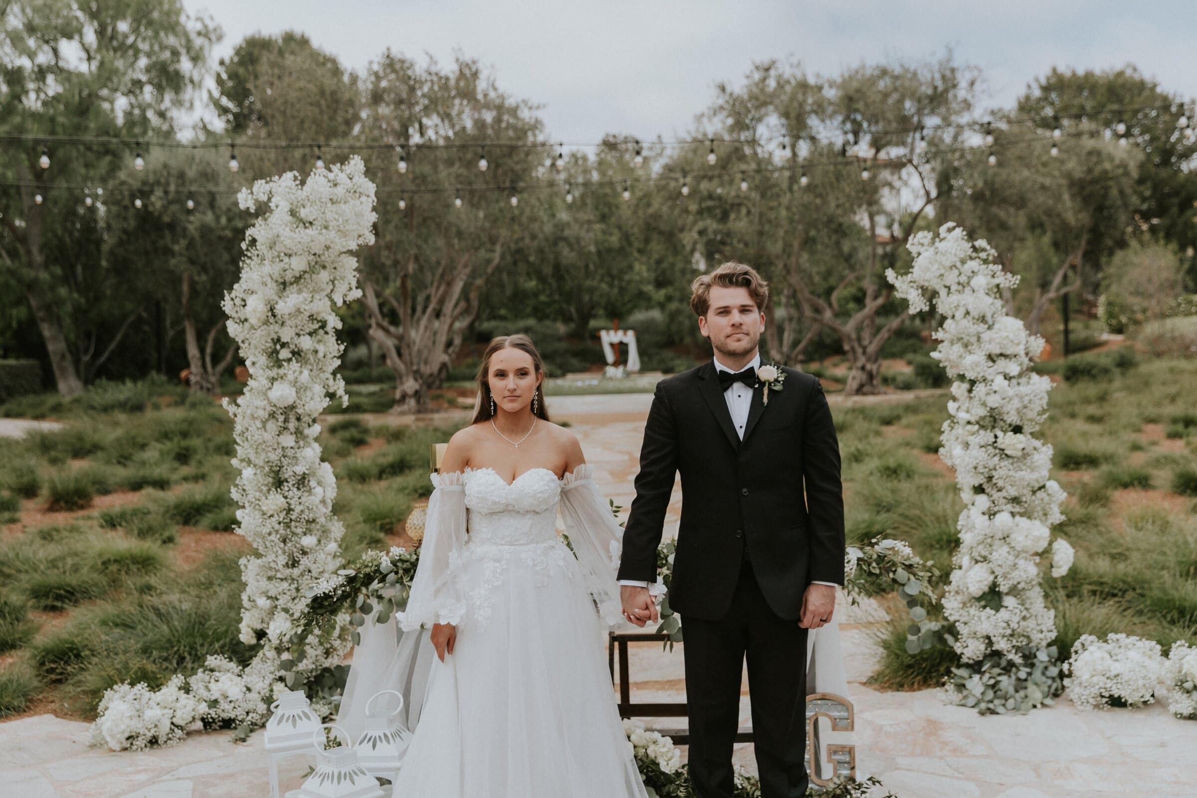 Irelyn and Aleck between two pillars of white flowers