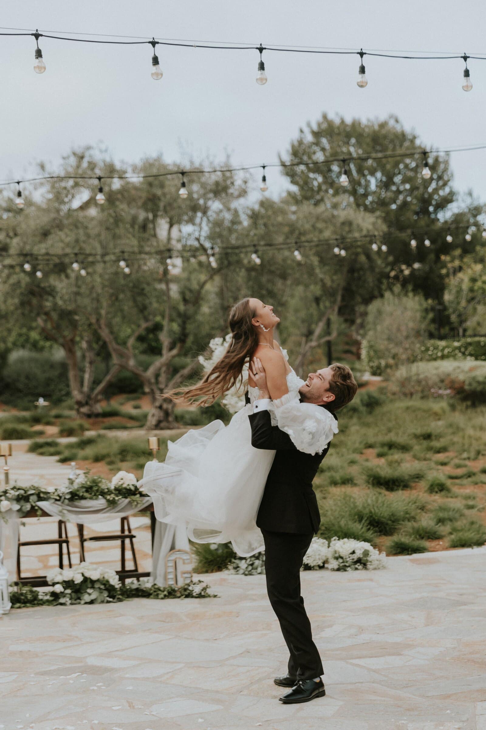 Aleck lifting Irelyn off the ground beneath string lights