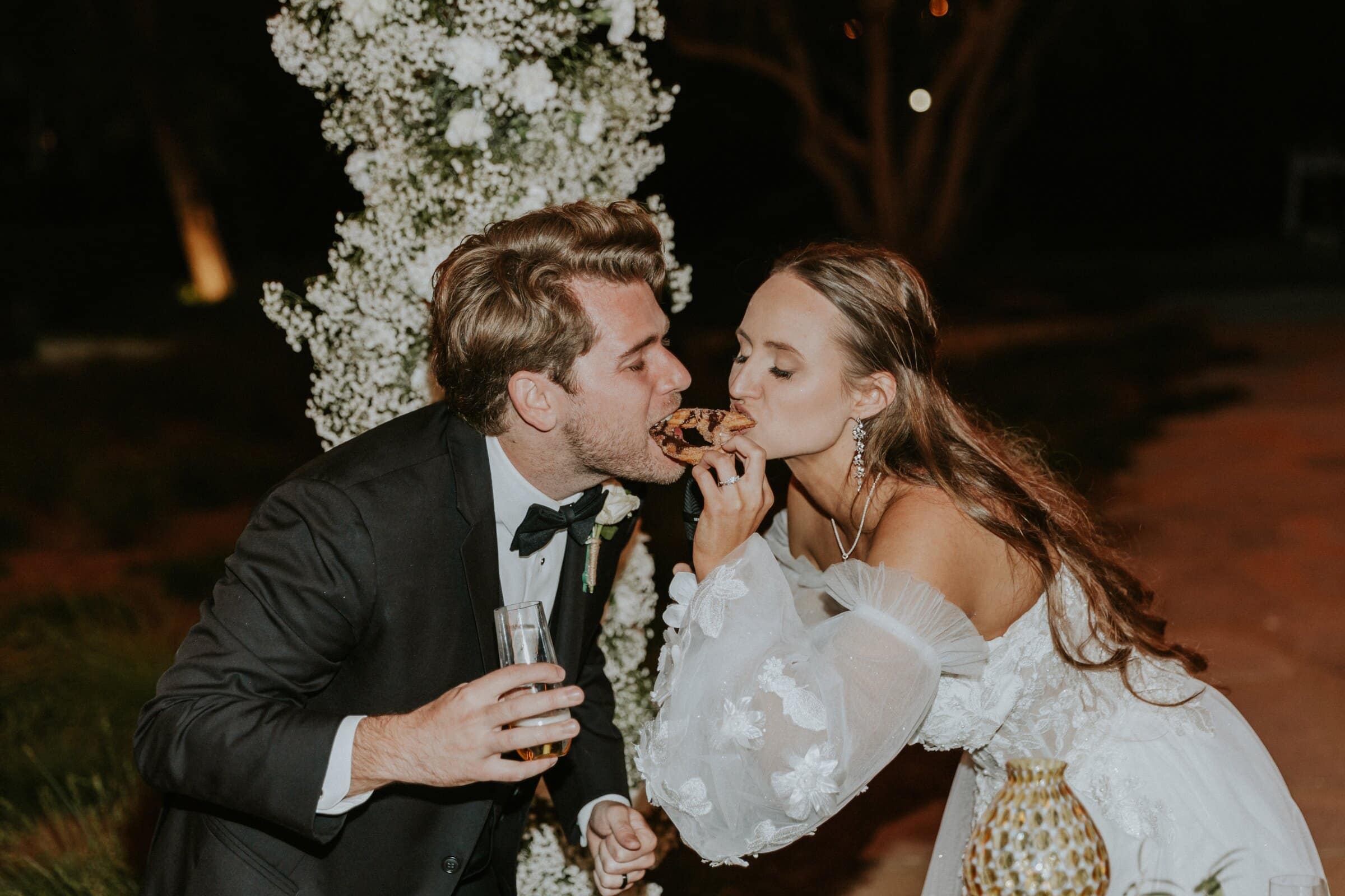 Aleck and Irelyn sharing a bite at night beside the white flowers