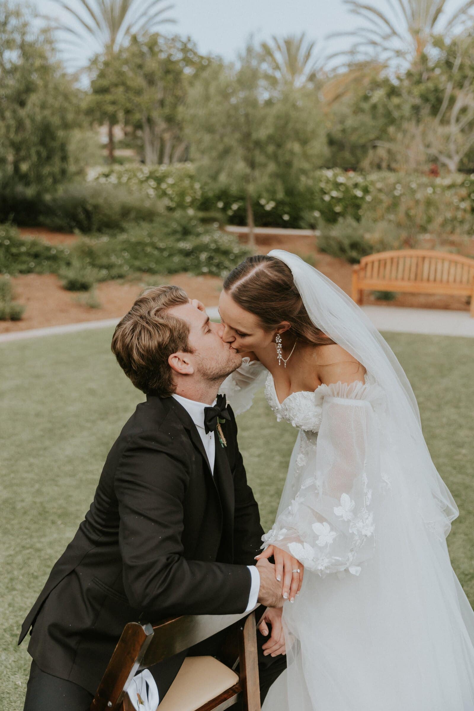 Irelyn leaning down to kiss Aleck as he sits on a wooden chair