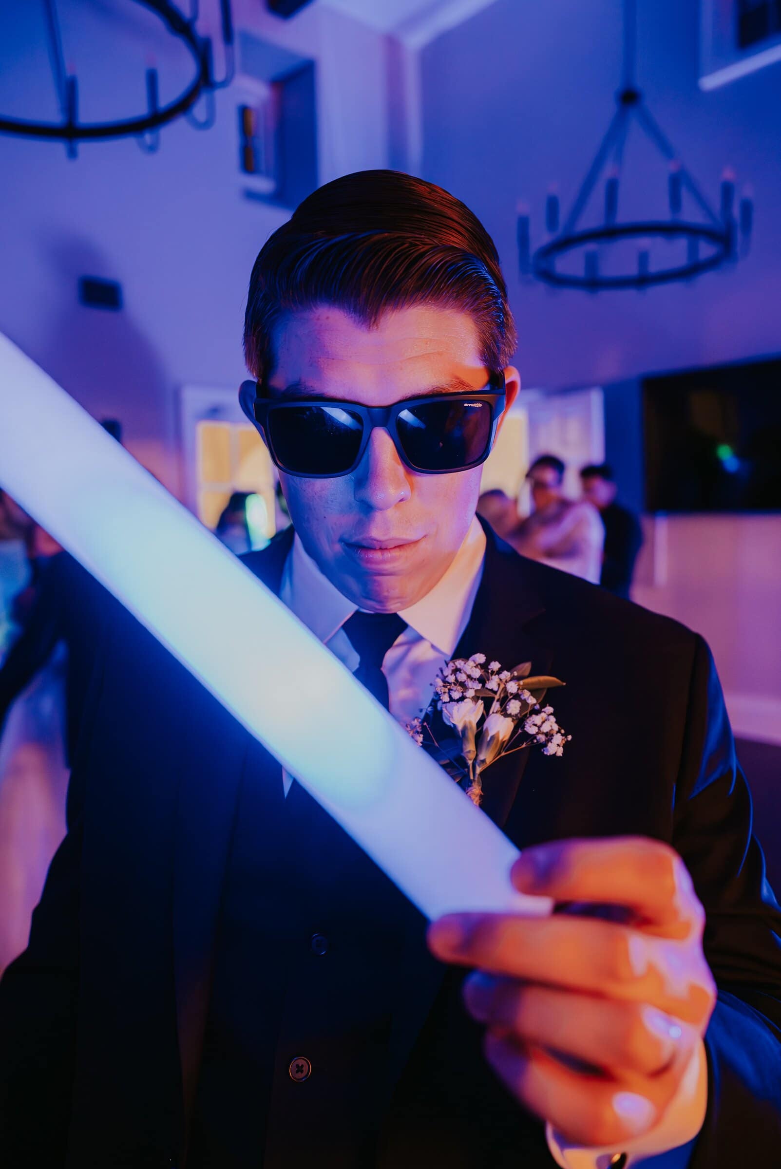 A groomsman in sunglasses holding up a glowing light stick