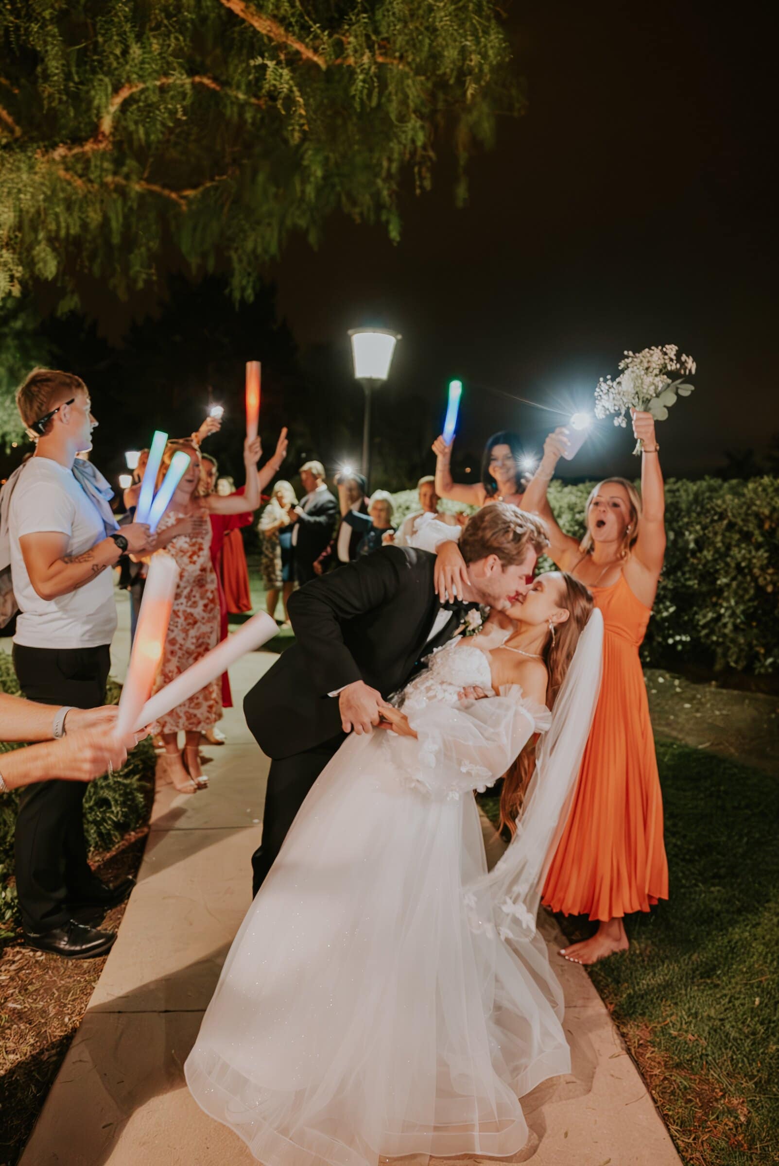 Aleck dipping Irelyn for a kiss as guests wave glow sticks at the send-off
