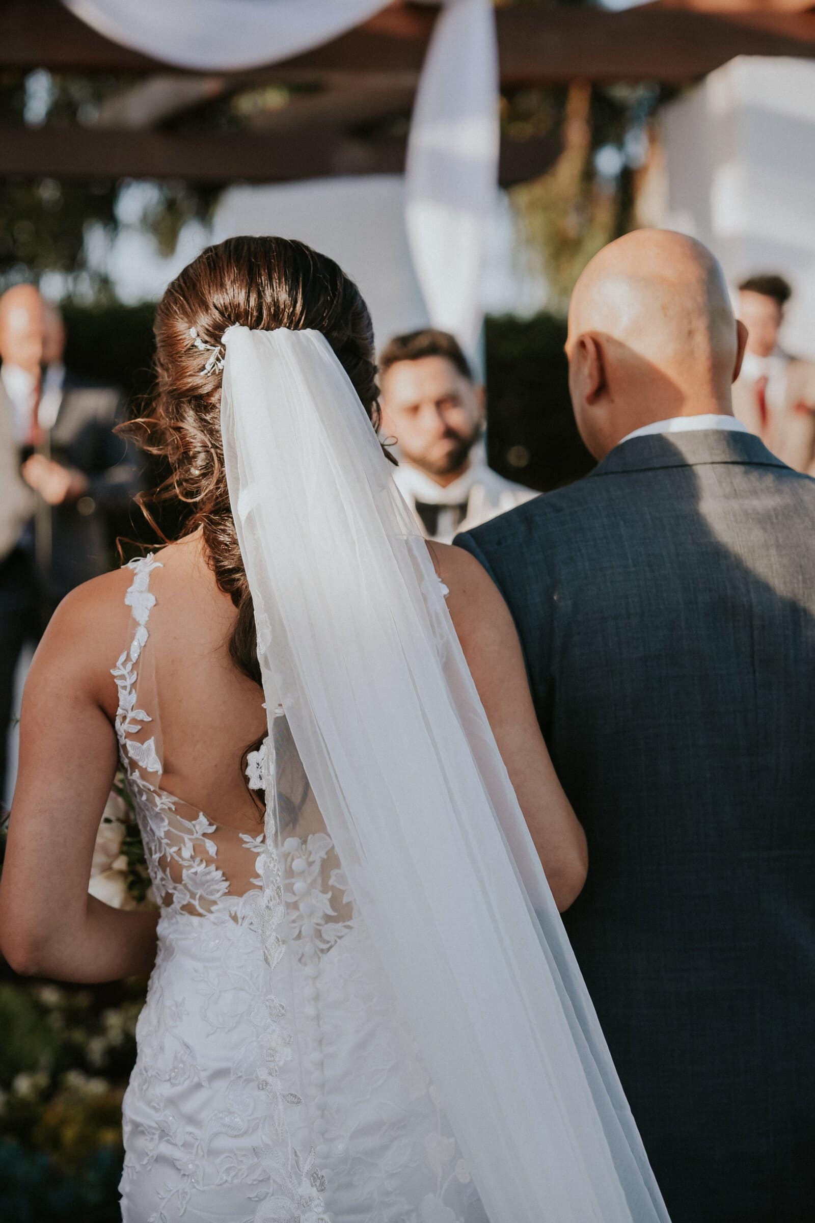 Ariana at the end of the aisle, her veil falling down her lace back