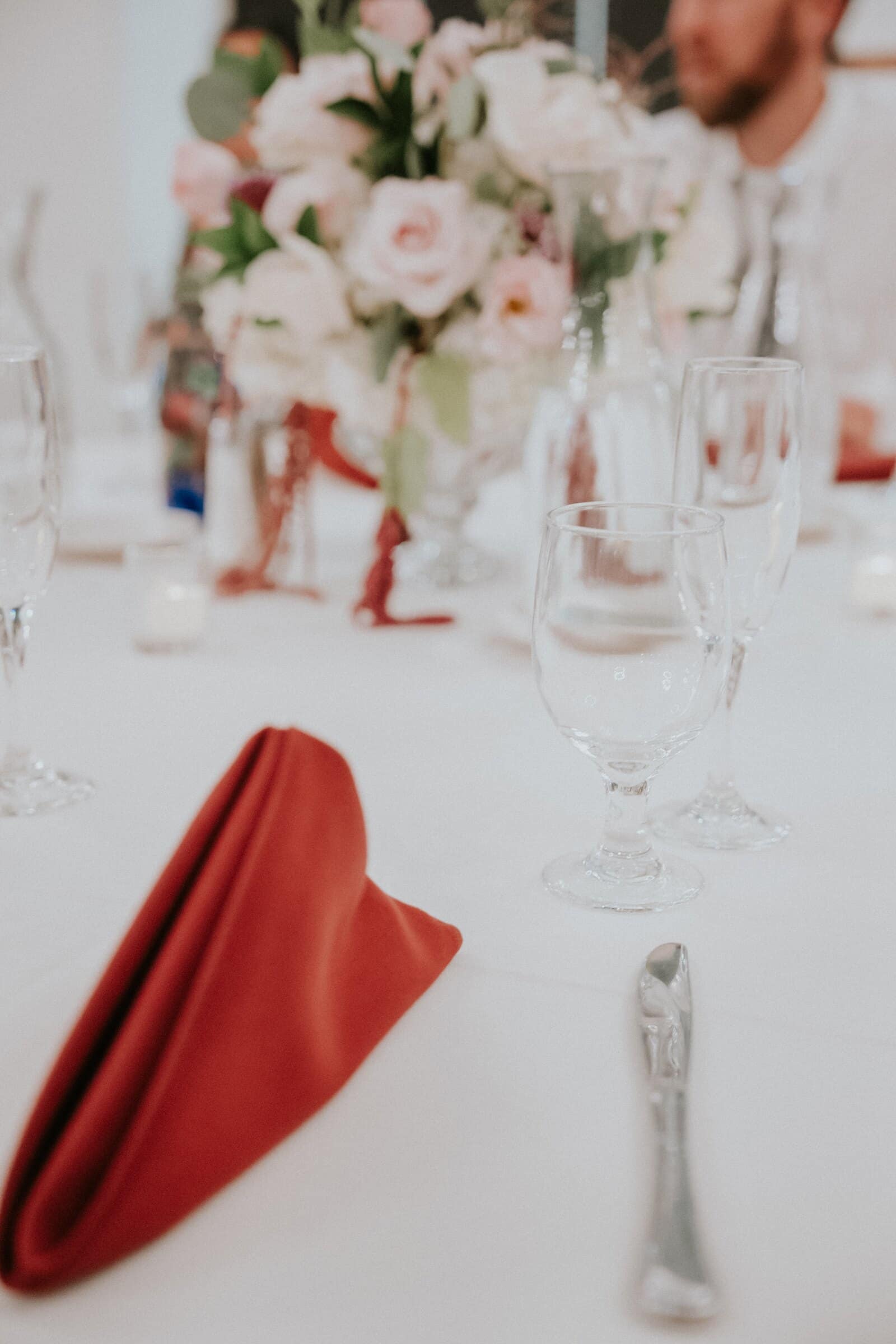 A red napkin and blush roses on a reception table
