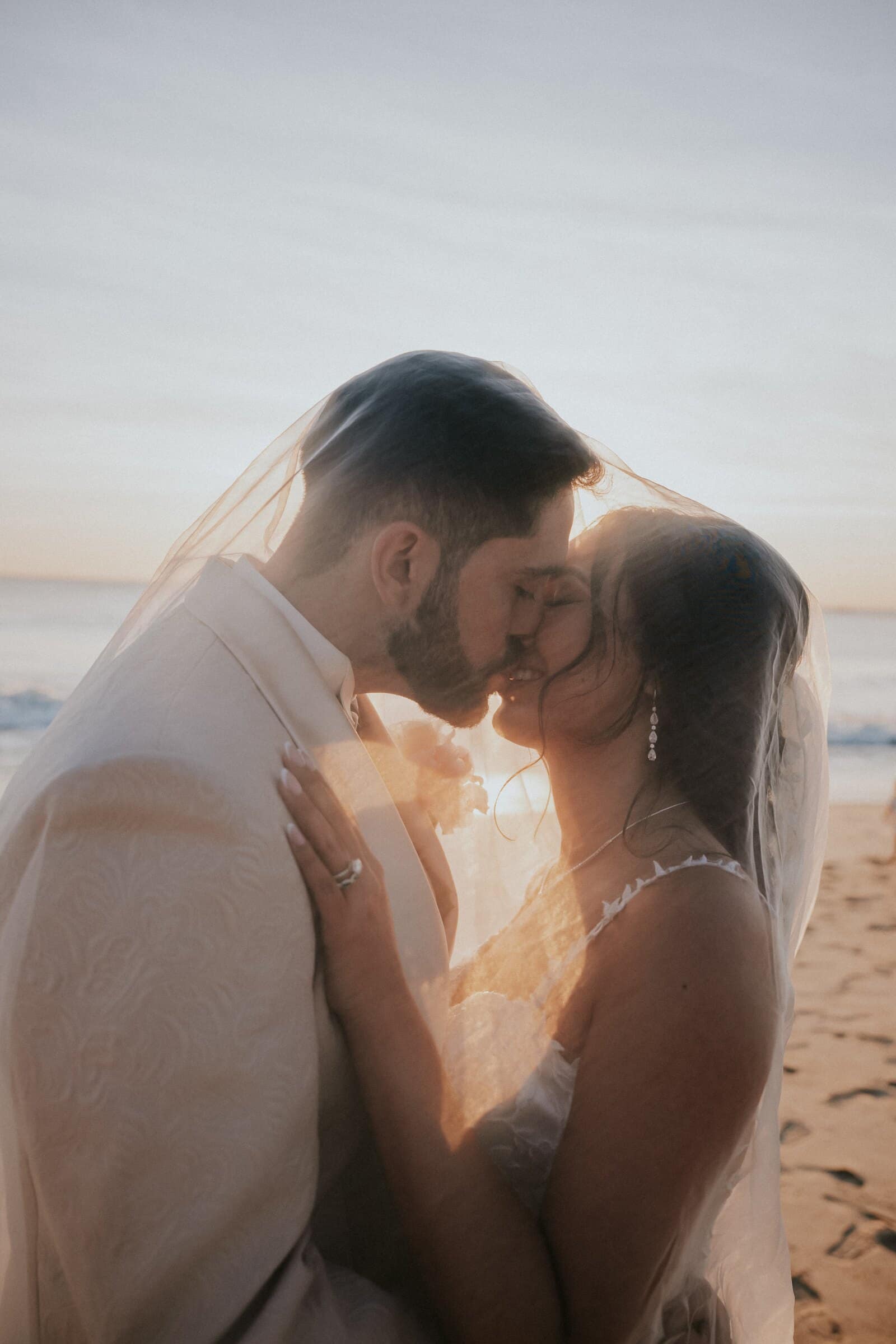 Dom and Ariana kissing beneath her veil with the sun behind them