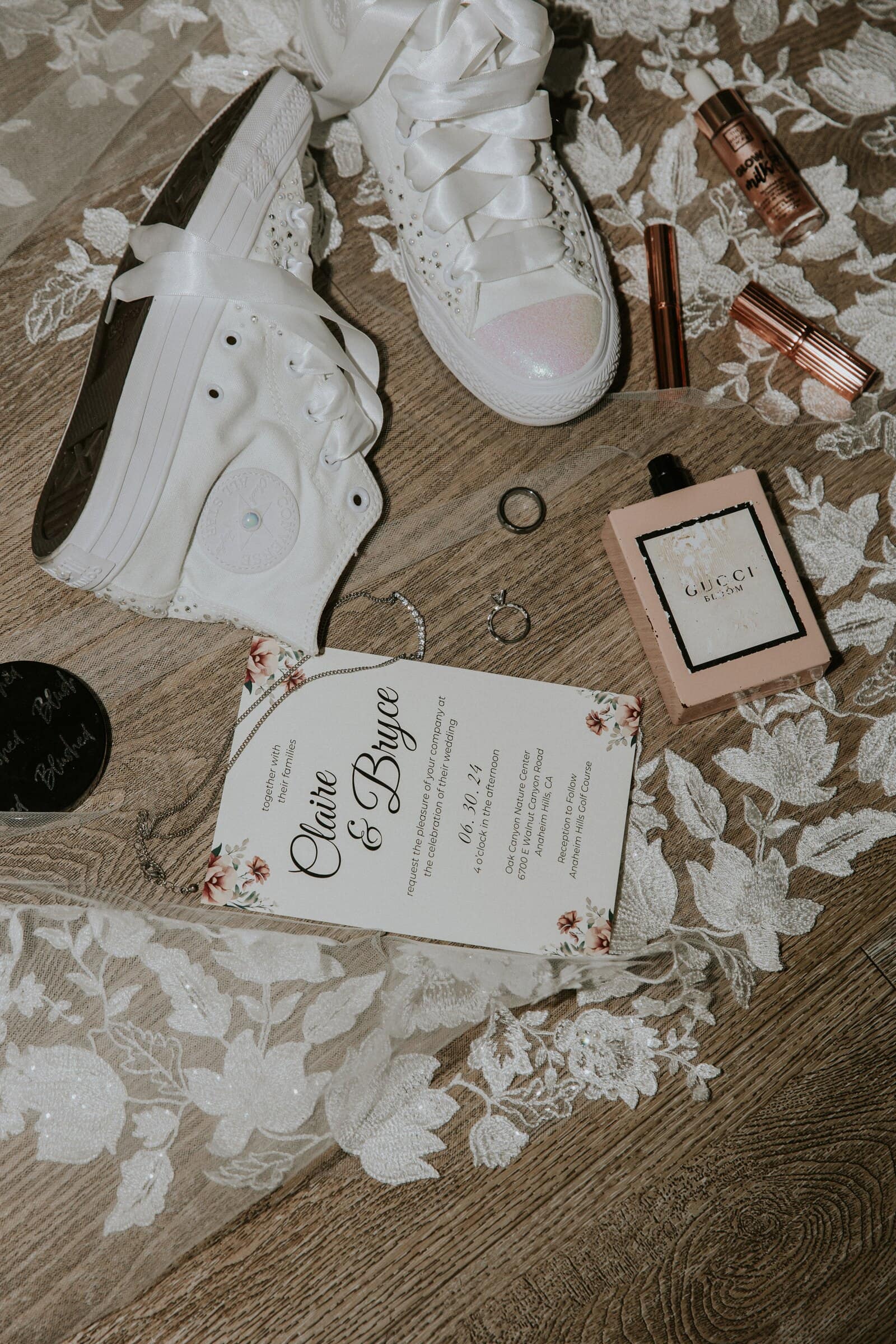 White high-top sneakers, perfume and the invitation laid on lace