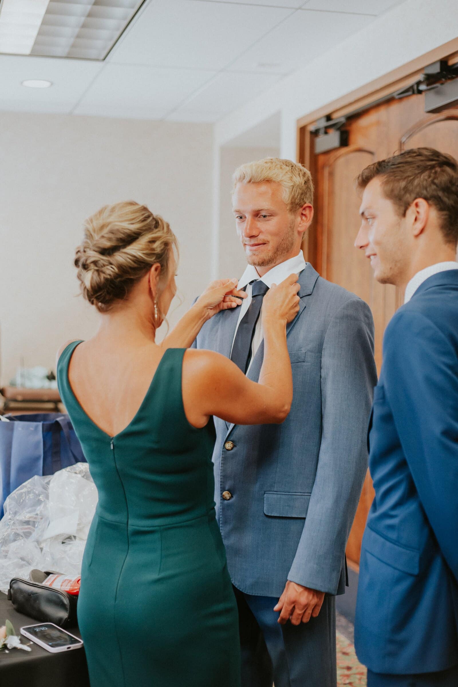 A woman in green pinning a boutonniere on a groomsman