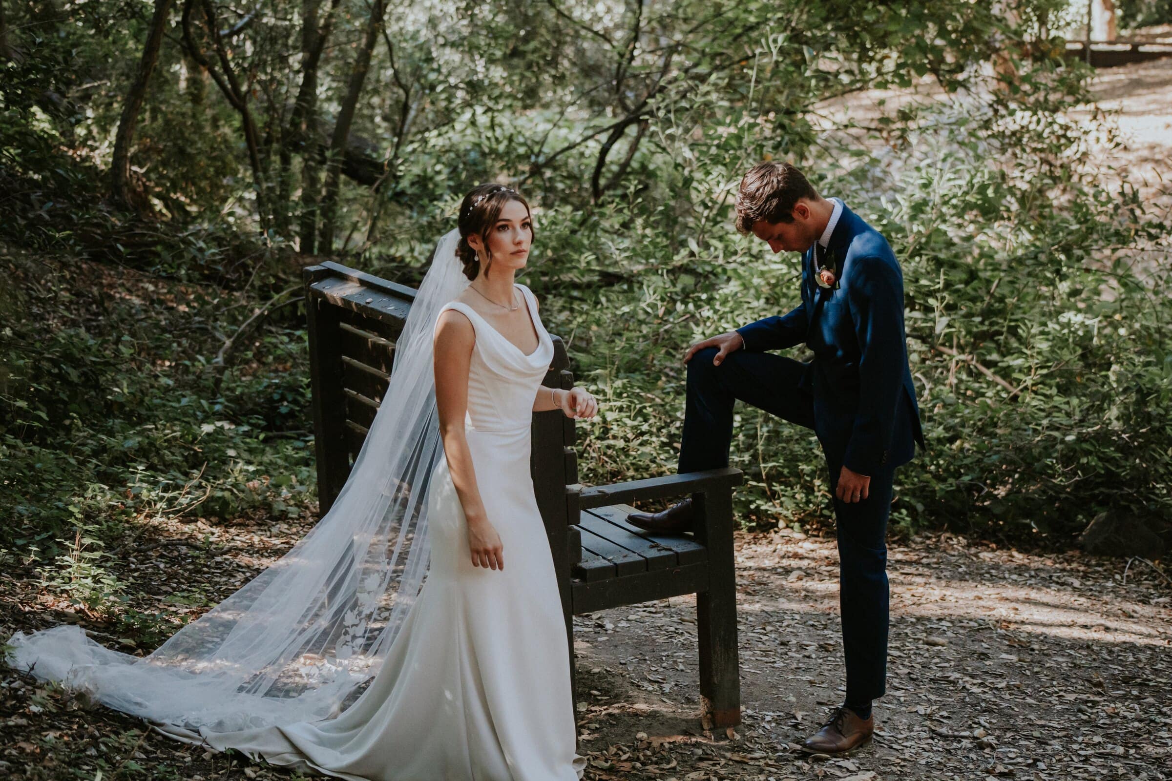 Bryce fixing his shoe on a bench while Claire waits, her veil trailing