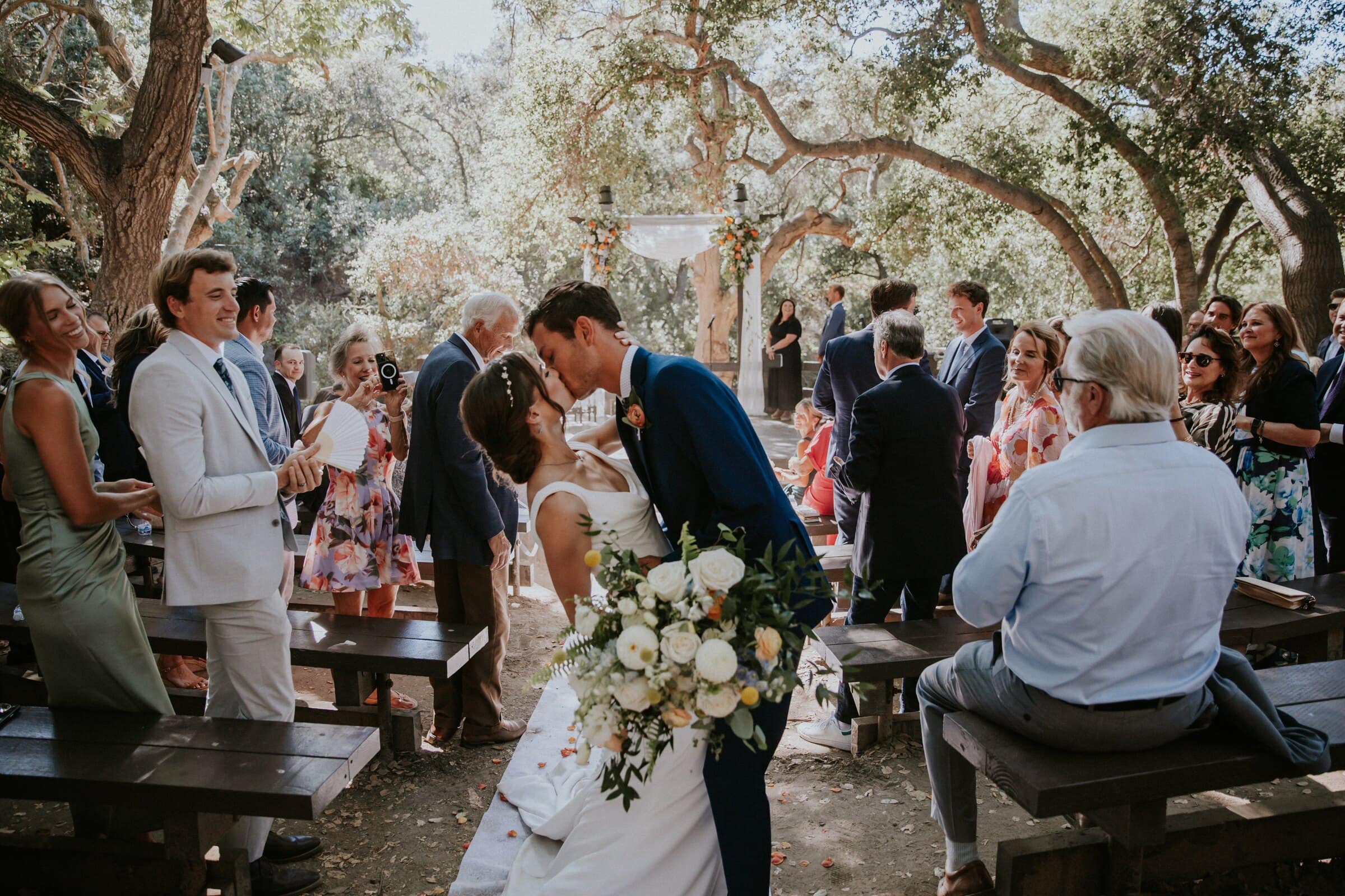 Bryce and Claire kissing in the aisle as guests stand around them