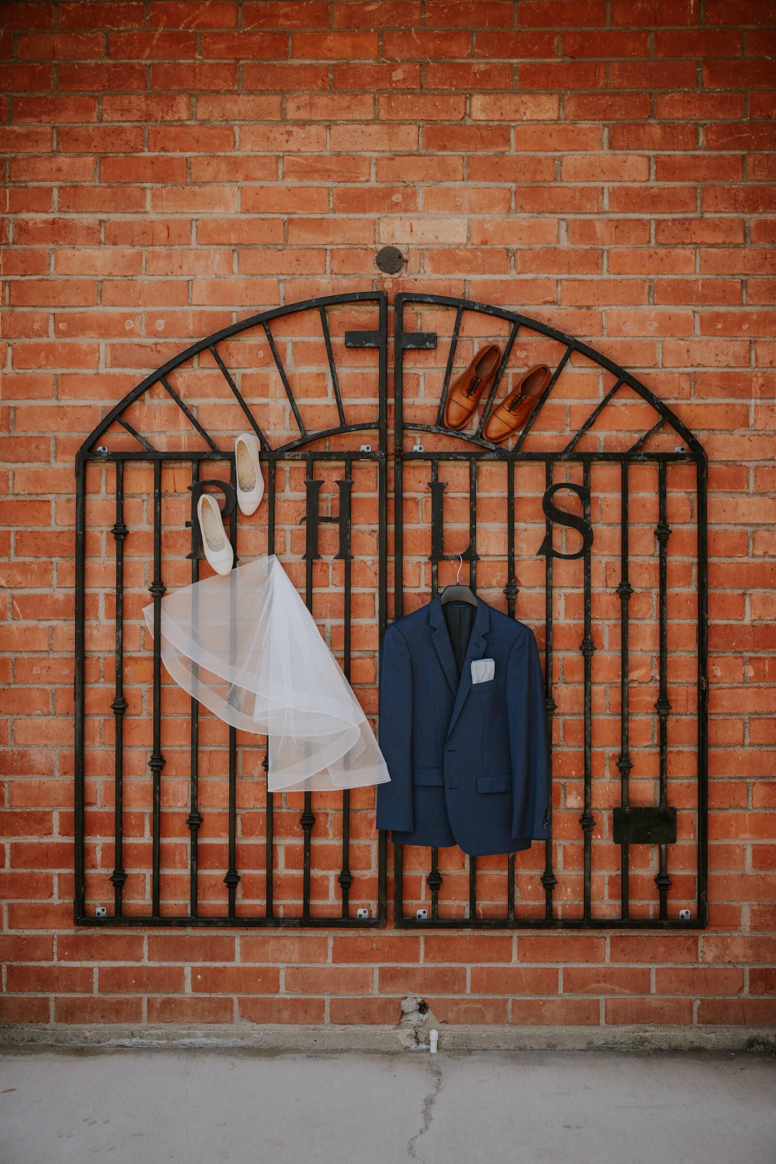 The veil and the groom's navy jacket hanging on an iron gate against a brick wall