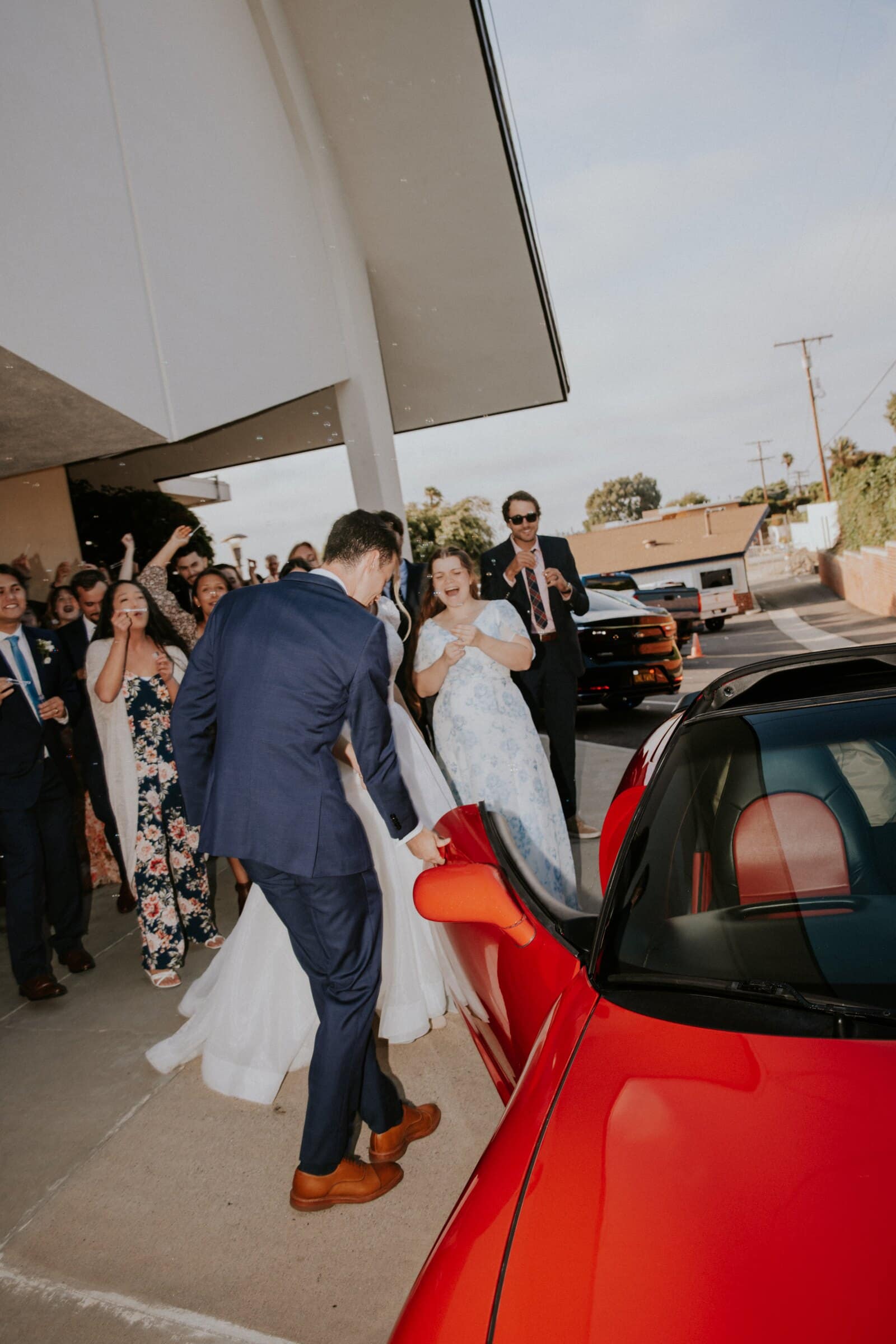 Morgan and Bryce climbing into a red convertible as guests cheer