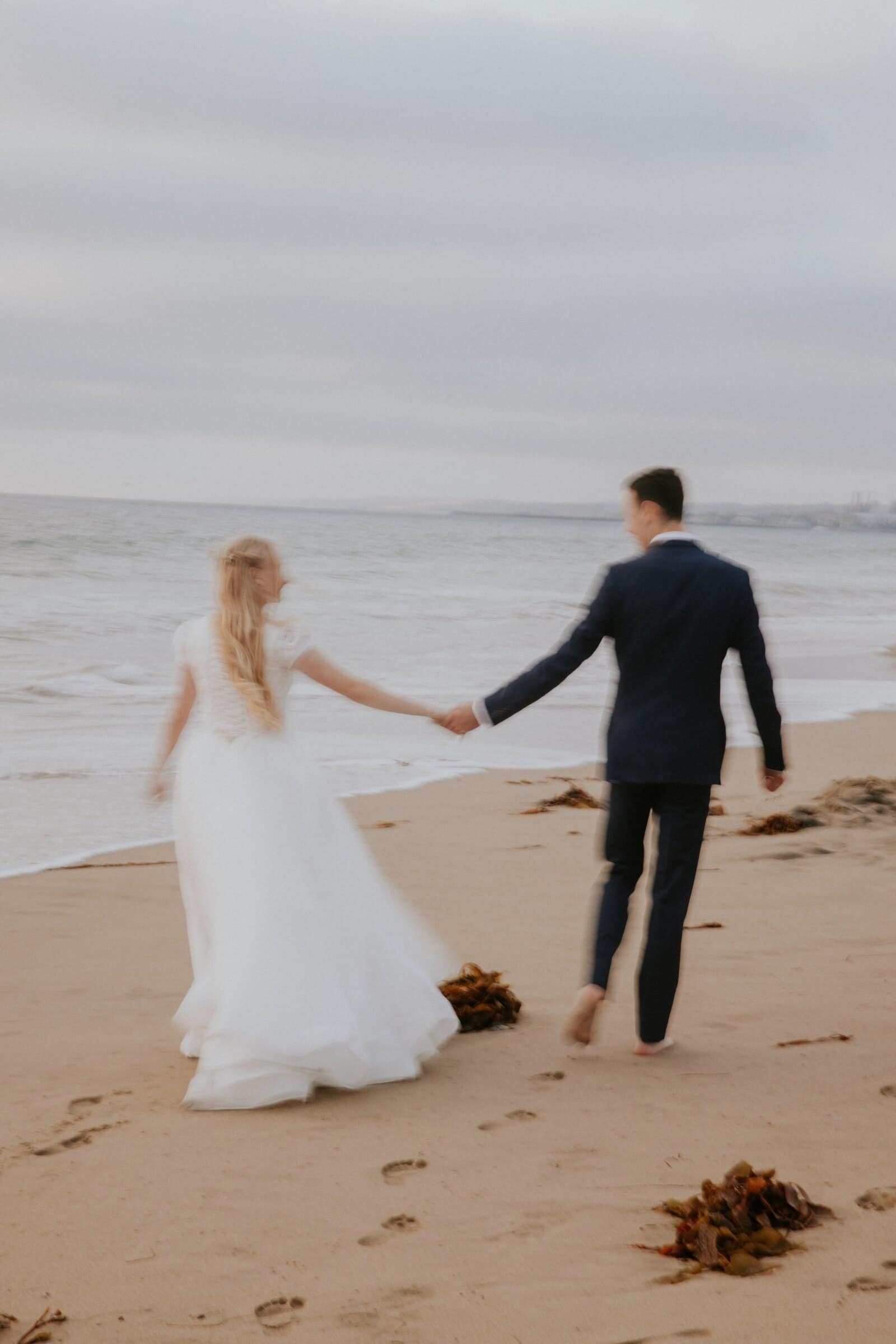 Morgan and Bryce walking hand in hand along the shore, seen from behind