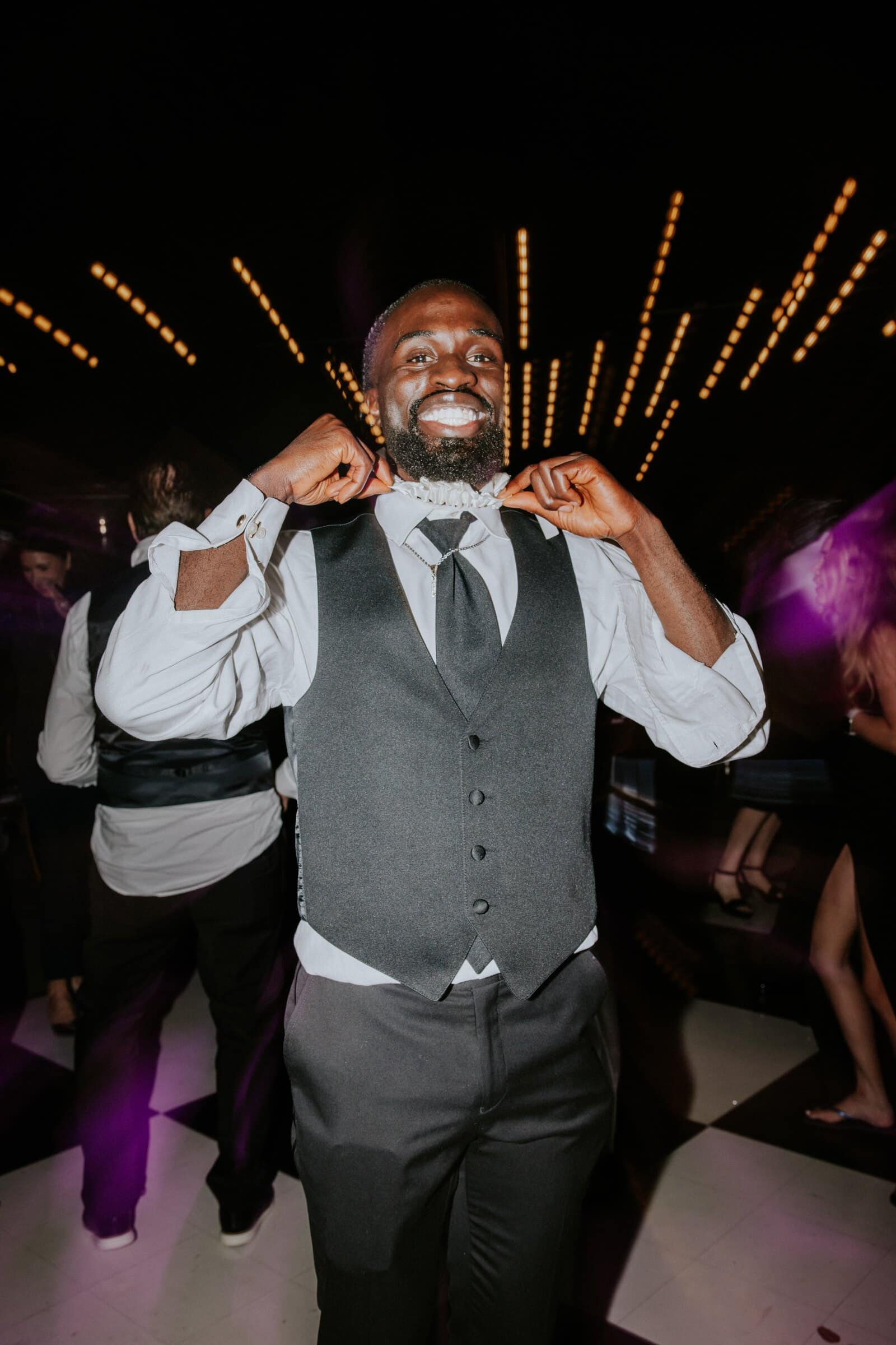 A guest in a grey vest dancing as the string lights streak behind him