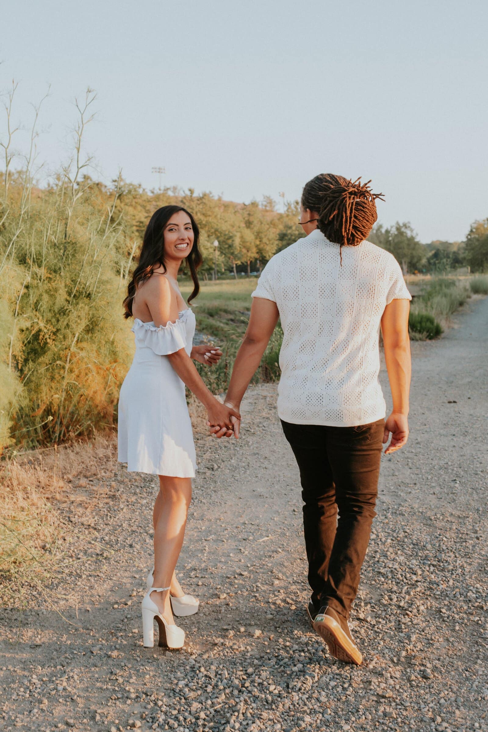 Jeremy and Ambica walking hand in hand down a gravel trail, seen from behind