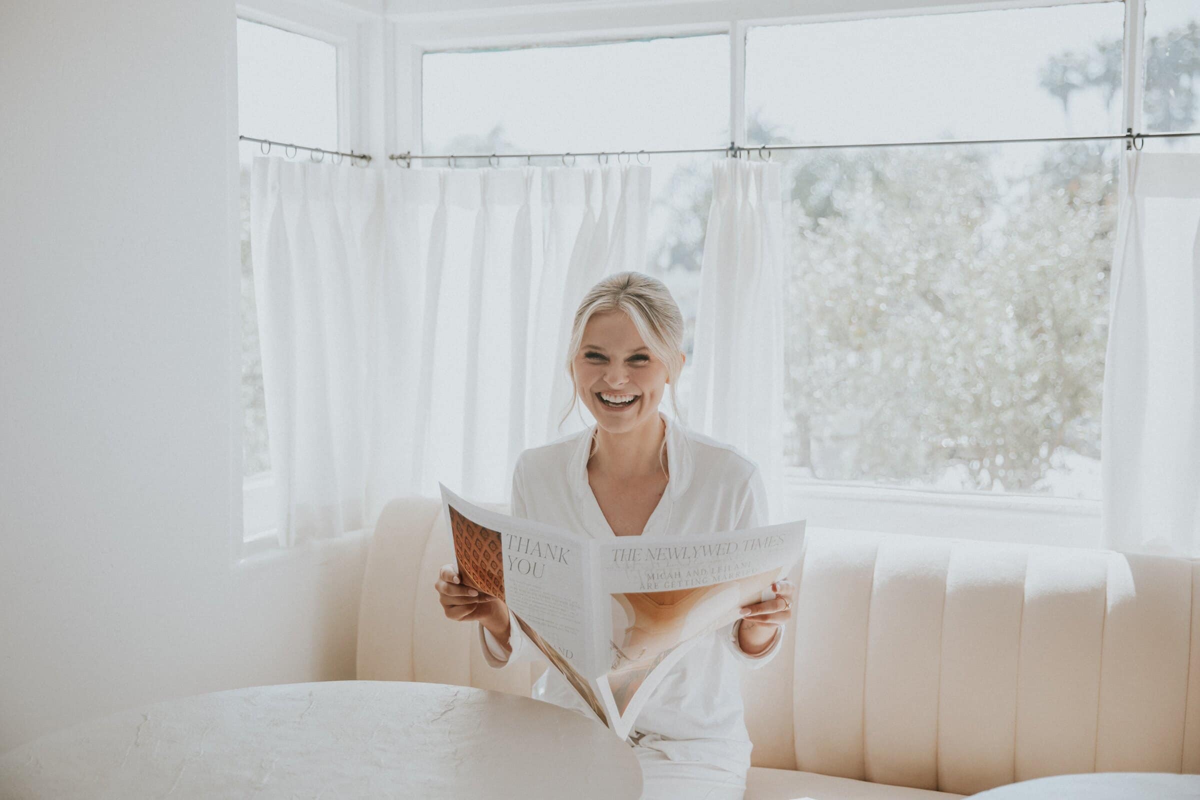 Leilani laughing as she reads a newspaper by the window
