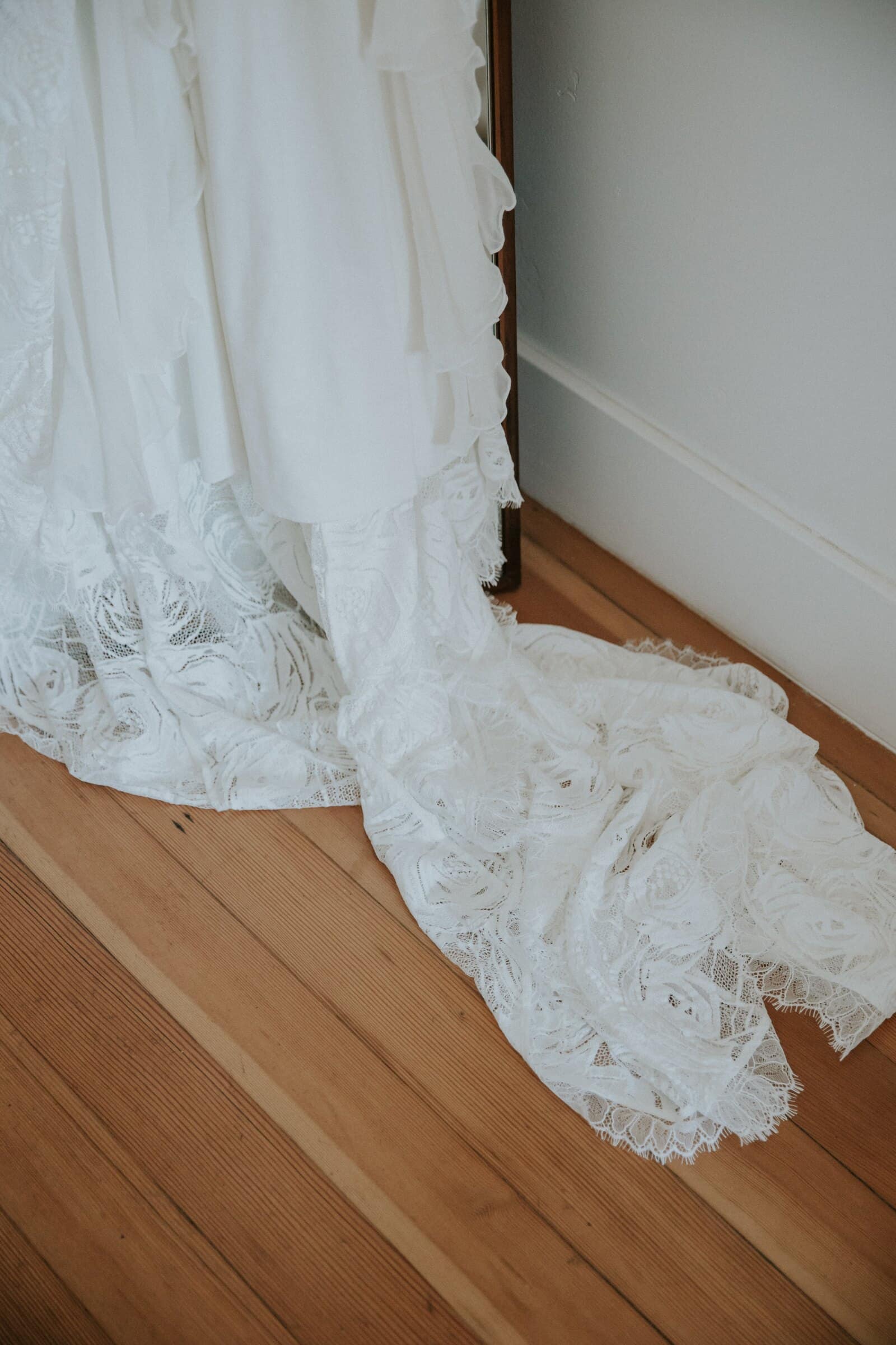 The lace train of the wedding dress pooled on a wooden floor