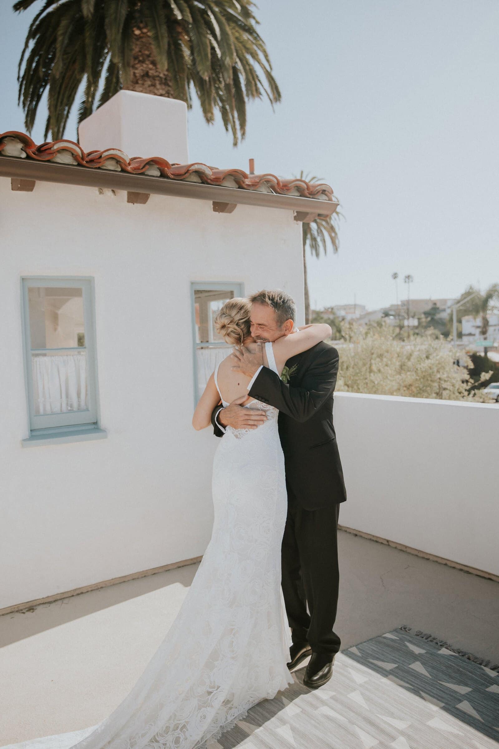 Leilani hugging a man in a dark suit on a white balcony