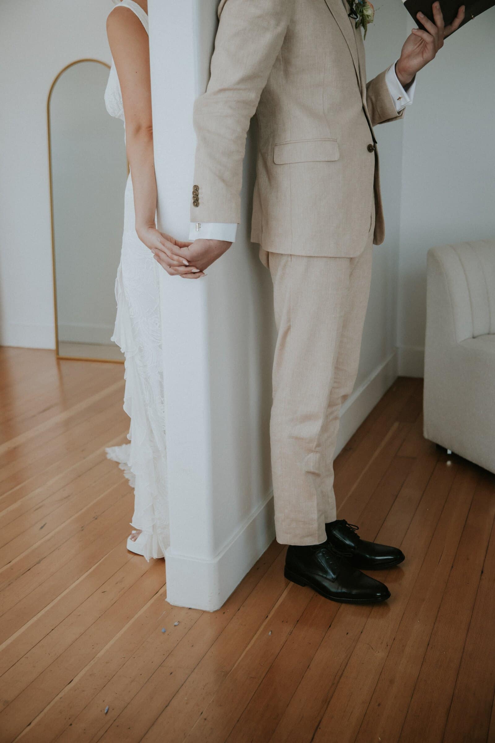 Micah and Leilani holding hands around a wall without seeing each other