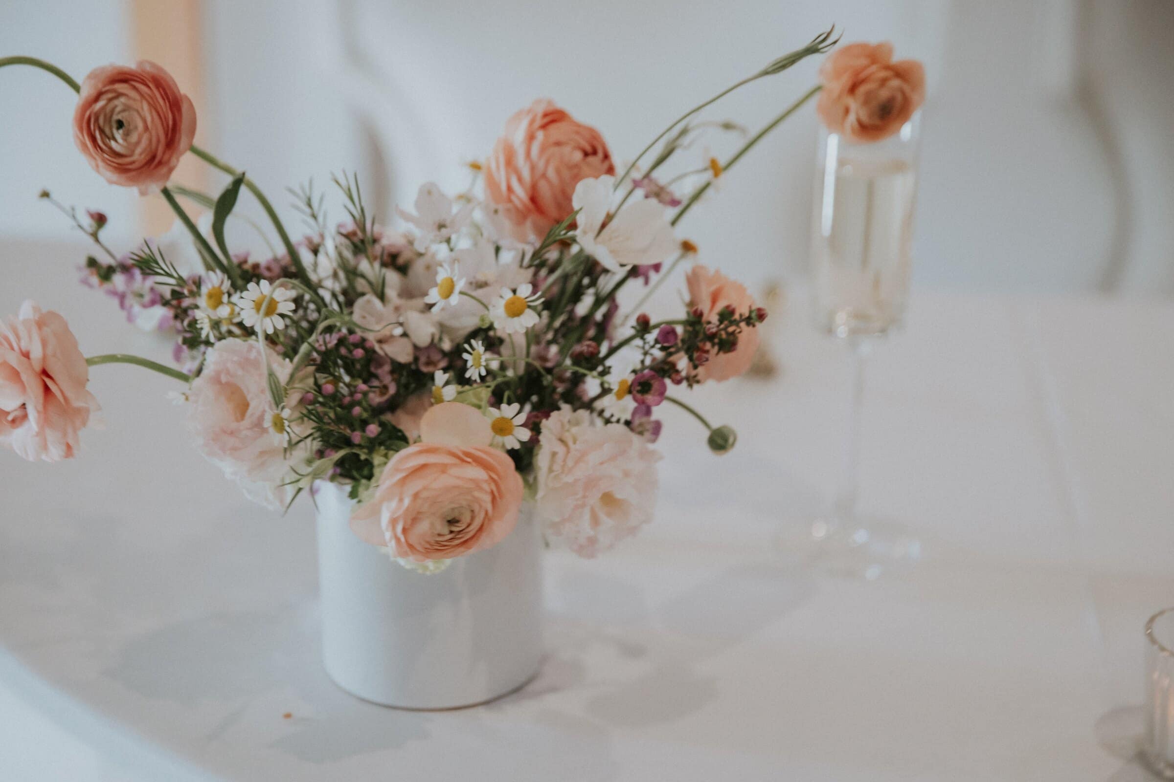 Peach ranunculus and wildflowers in a white vase