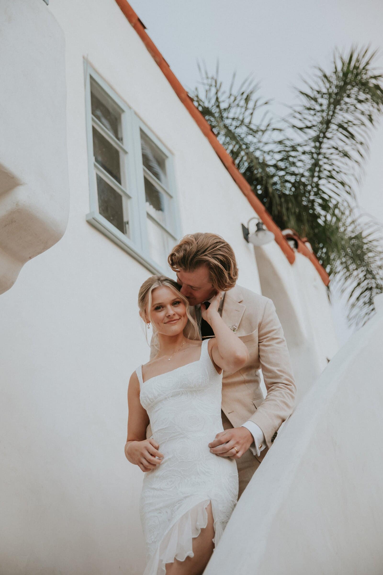 Micah kissing Leilani's temple against a white stucco wall