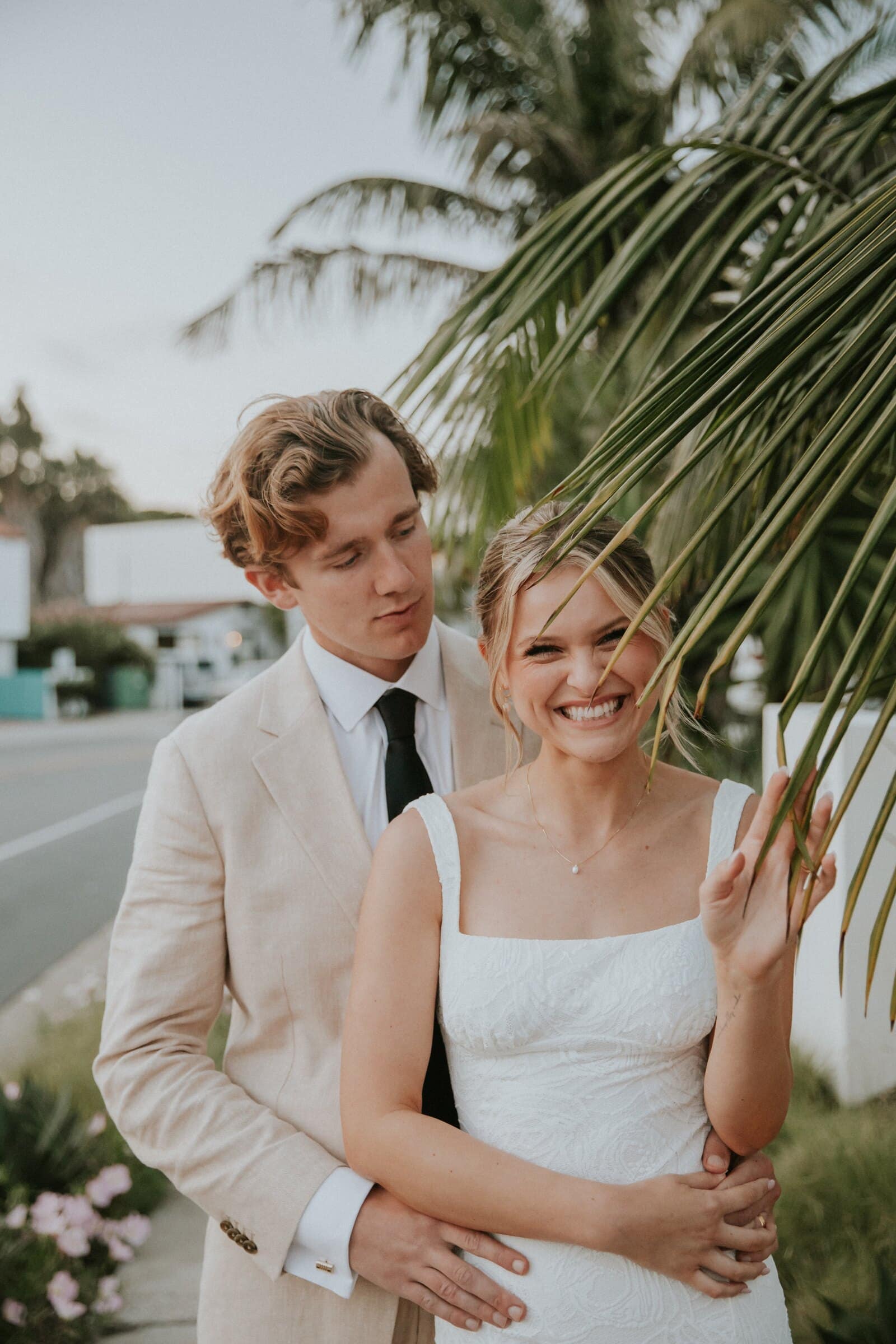 Micah holding Leilani from behind beside a palm frond