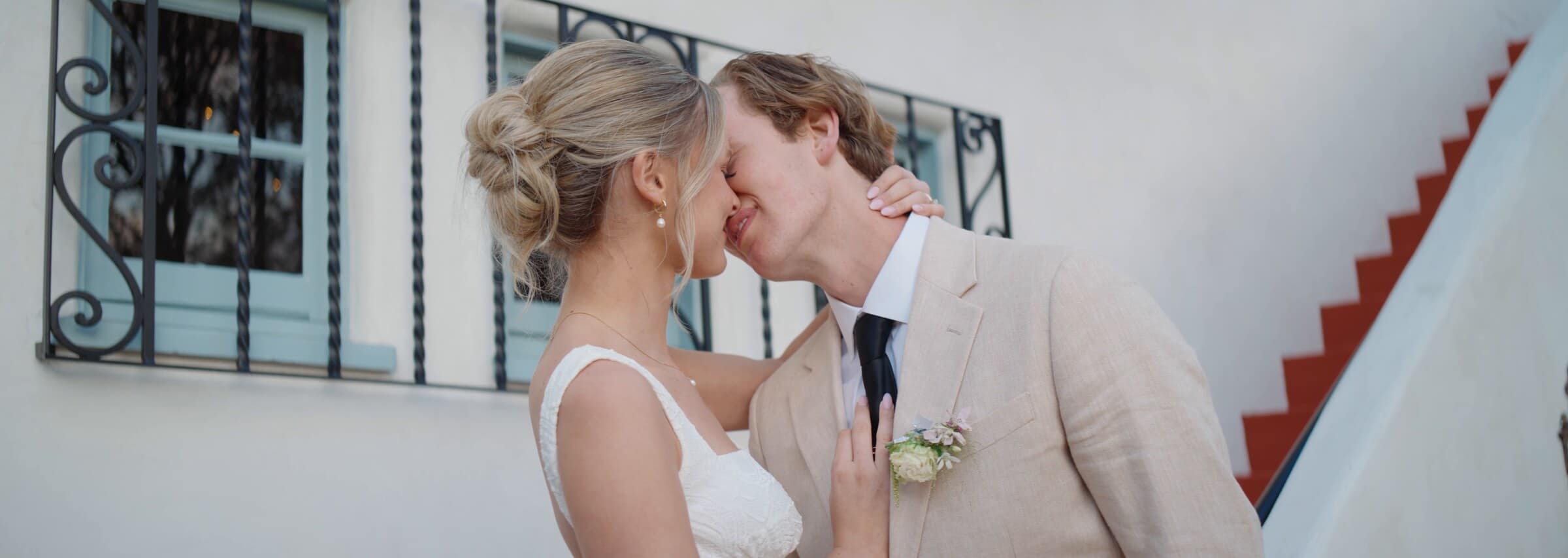 Micah and Leilani kissing beside a white wall and a red-tiled staircase