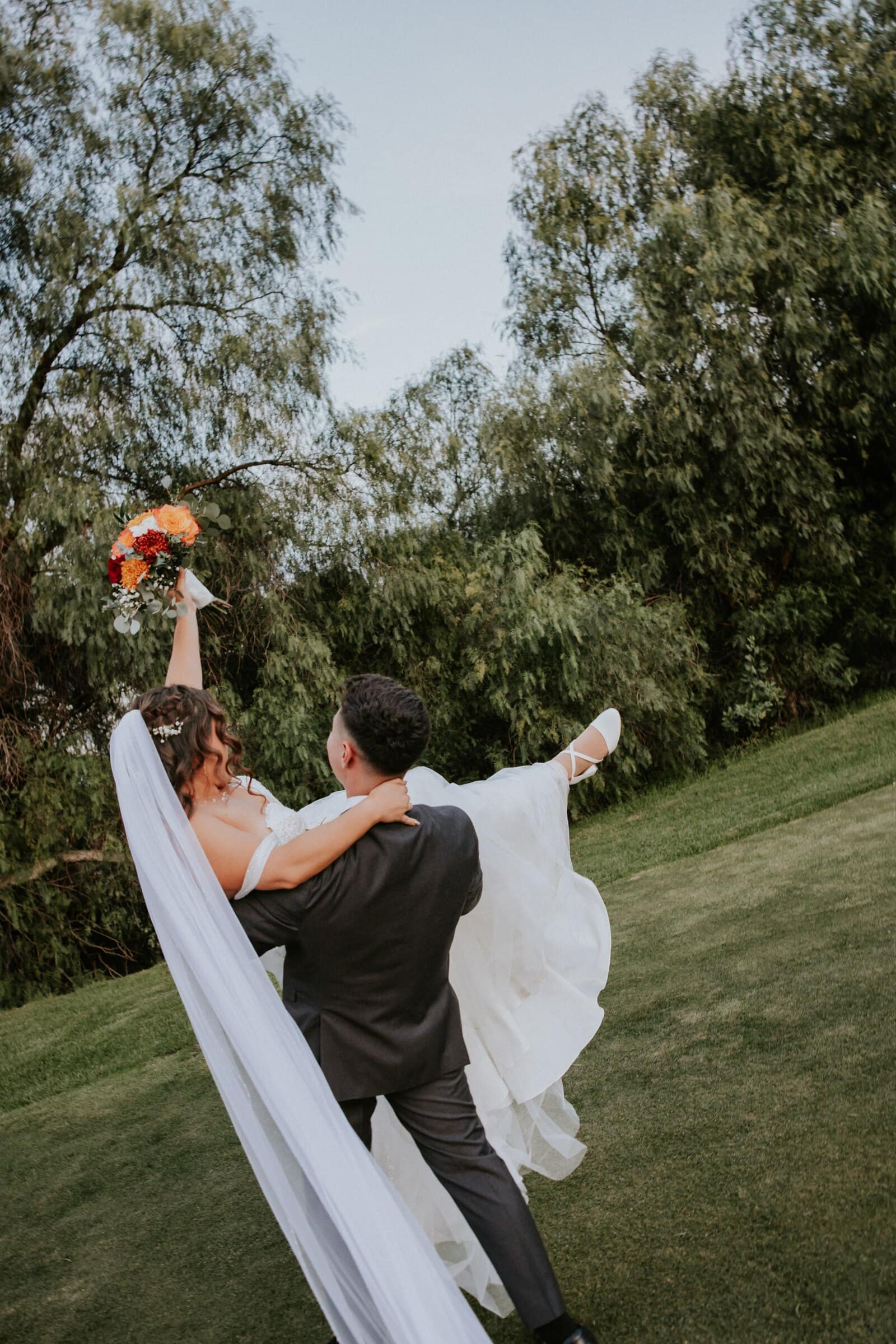 Natalie's veil flying as David lifts her on the lawn